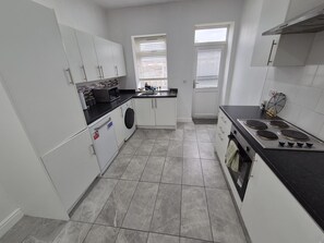 A compact kitchen with white cabinets, a built-in oven, a microwave, and a stove. - 3 Bed House-Sleeps 8-Families-Contractors-NHS-Garden-Parking-Fast WiFi (Willenhall)