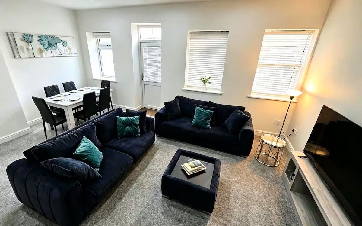 A living room with two dark sofas, a coffee table, a dining table with chairs, and a TV.