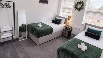 A hotel room with two beds, a wardrobe, a mirror, a cityscape painting, and a window with blinds.