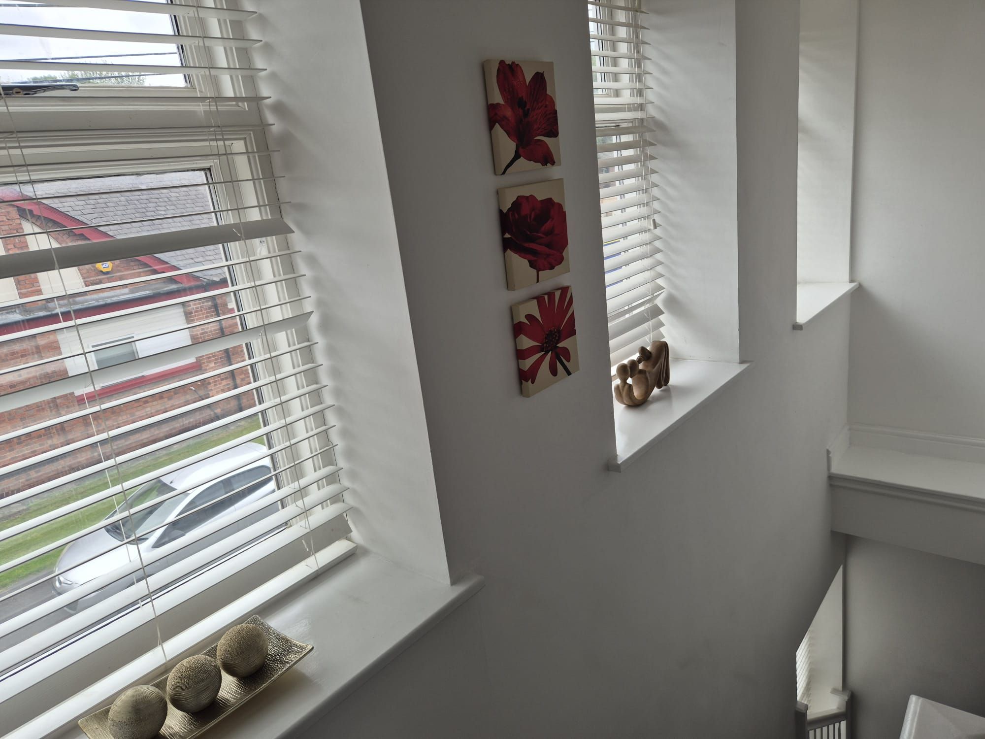 A room with a large window, a white wall, and a small shelf with decorative items.