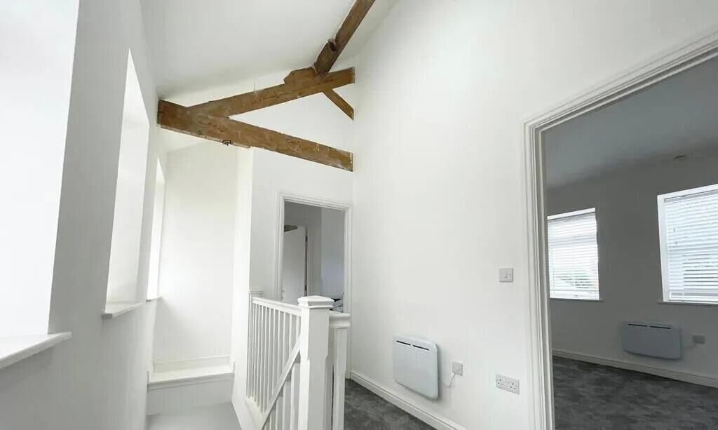Quarto com paredes brancas, um vigamento de madeira no teto, radiador branco e uma janela com persianas.