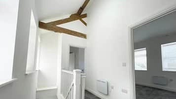 Quarto com paredes brancas, um vigamento de madeira no teto, radiador branco e uma janela com persianas.