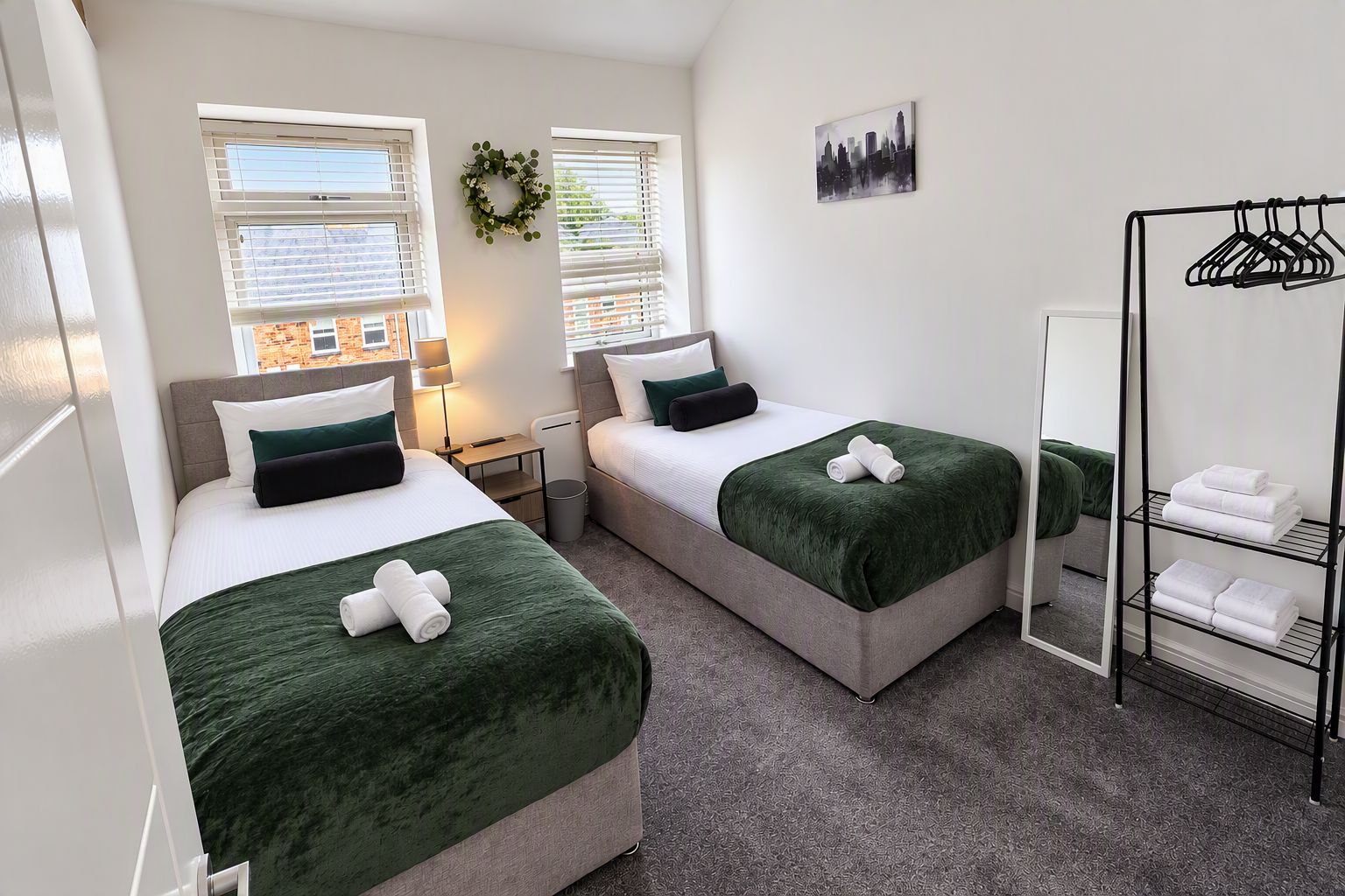 A hotel room with two beds, a mirror, a towel rack, and a view of the cityscape.