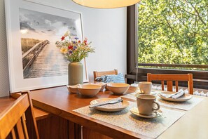 Un comedor con una mesa de madera, cuencos, tazas y un florero con flores.
