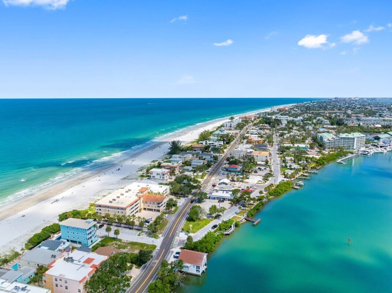 Vista aérea de un pueblo costero con playa, edificios residenciales y un puerto deportivo.