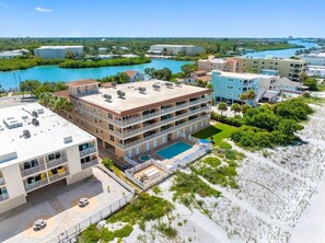 Een hotel met meerdere verdiepingen, een zwembad op het dak, omringd door groen en een strand.