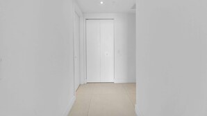 A narrow hallway with a closed white door at the end, white walls, and a tiled floor. - Waterfront Oasis With Resort Amenities (Hollywood)