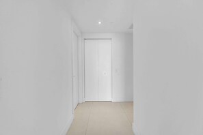 A narrow hallway with a closed white door at the end, white walls, and a tiled floor. - Waterfront Oasis With Resort Amenities (Hollywood)