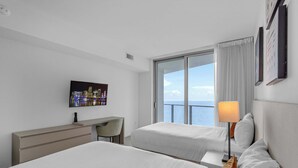 A hotel room with two beds, a desk, a chair, a TV, and a window with a view of the sea. - Waterfront Oasis With Resort Amenities (Hollywood)