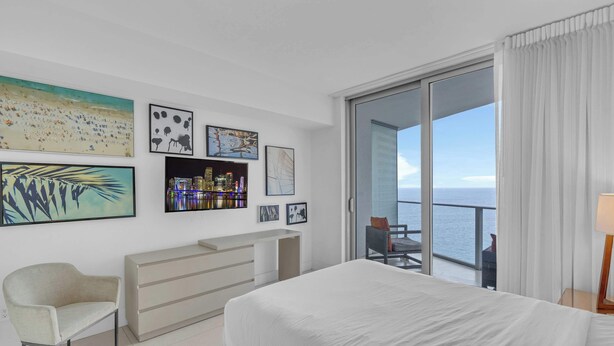 A hotel room with a bed, a chair, a desk, a balcony with a view of the sea, and artwork on the walls. - Waterfront Oasis With Resort Amenities (Hollywood)