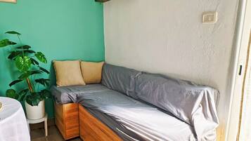 Een kleine kamer met een houten bed, een tafeltje, een potplant en een groen bordje dat een rokersruimte aangeeft.