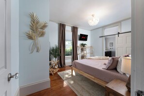 Ein Schlafzimmer mit Bett, Fernseher, Pflanze und Tür.