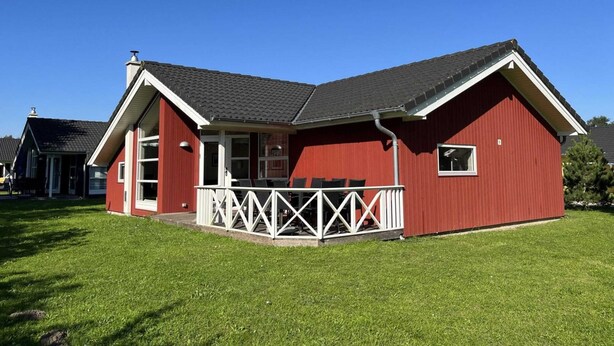 Une maison rouge à un seul étage, avec un porche blanc et un toit noir.