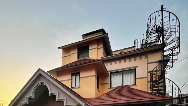 A two-story house with a red roof, a brick lower section, and a metal staircase on the right.