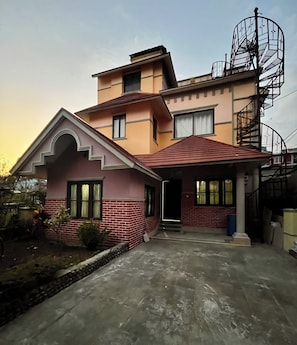 Une maison à deux étages avec un toit rouge, une partie inférieure en briques et un escalier métallique situé sur le côté droit.