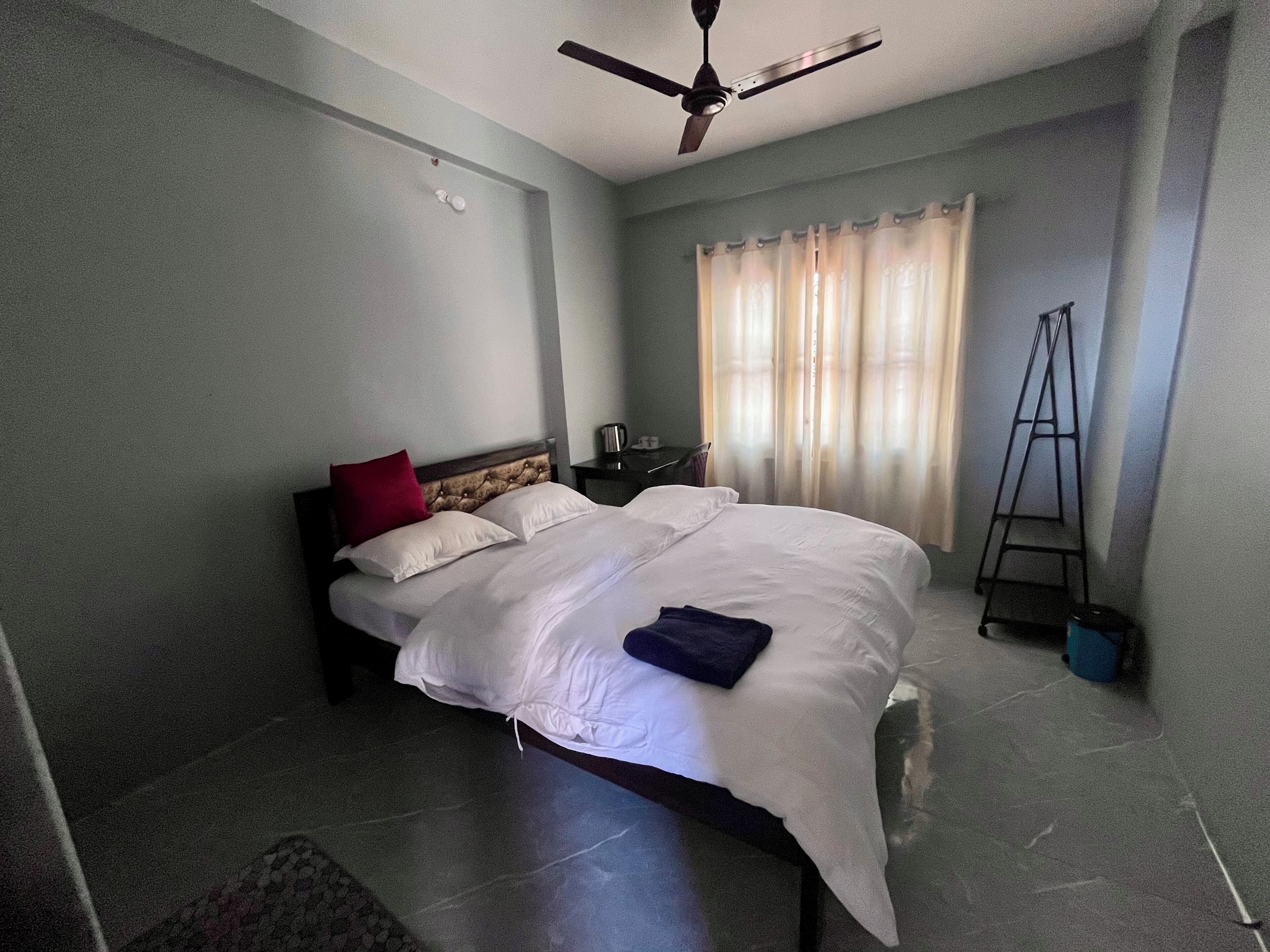 A bedroom with a bed, a ceiling fan, a window with curtains, and a ladder.