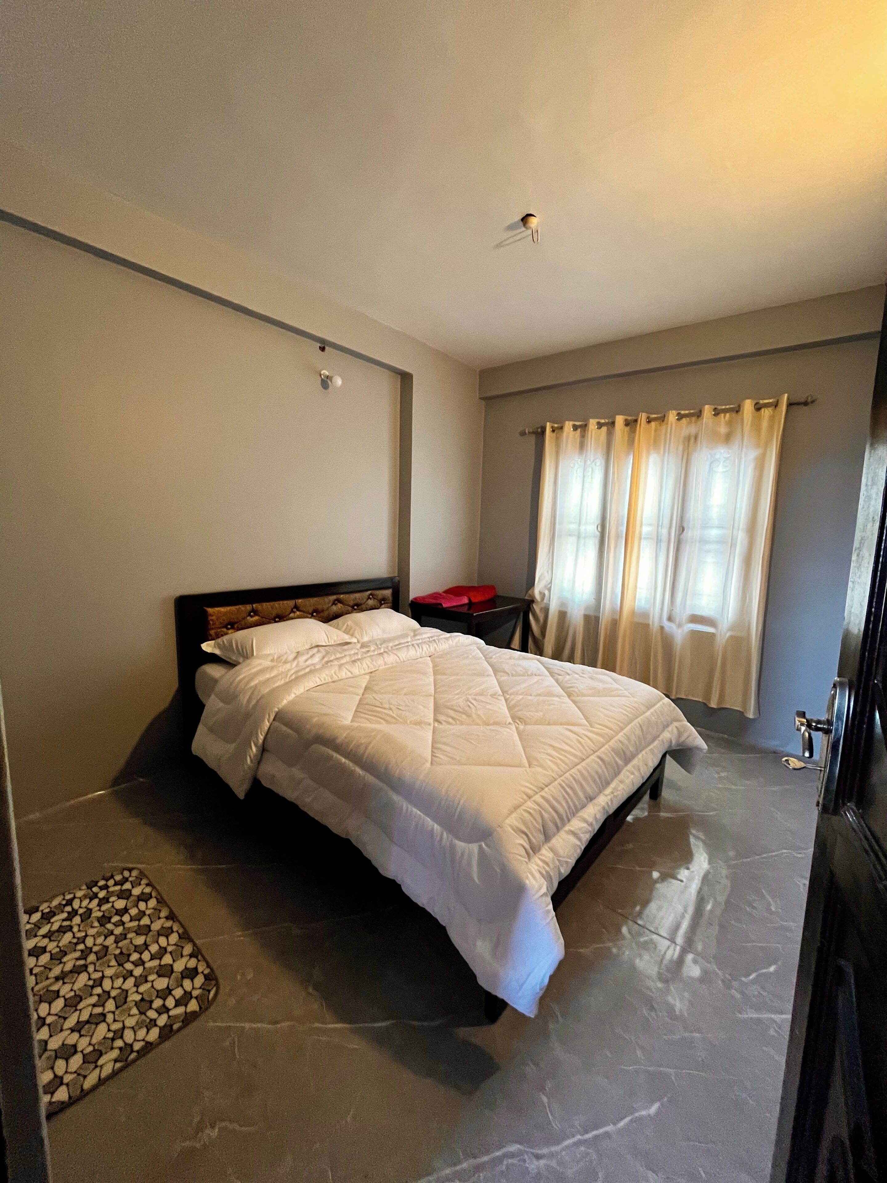 A bedroom with a bed, a nightstand, a window with curtains, and a door.
