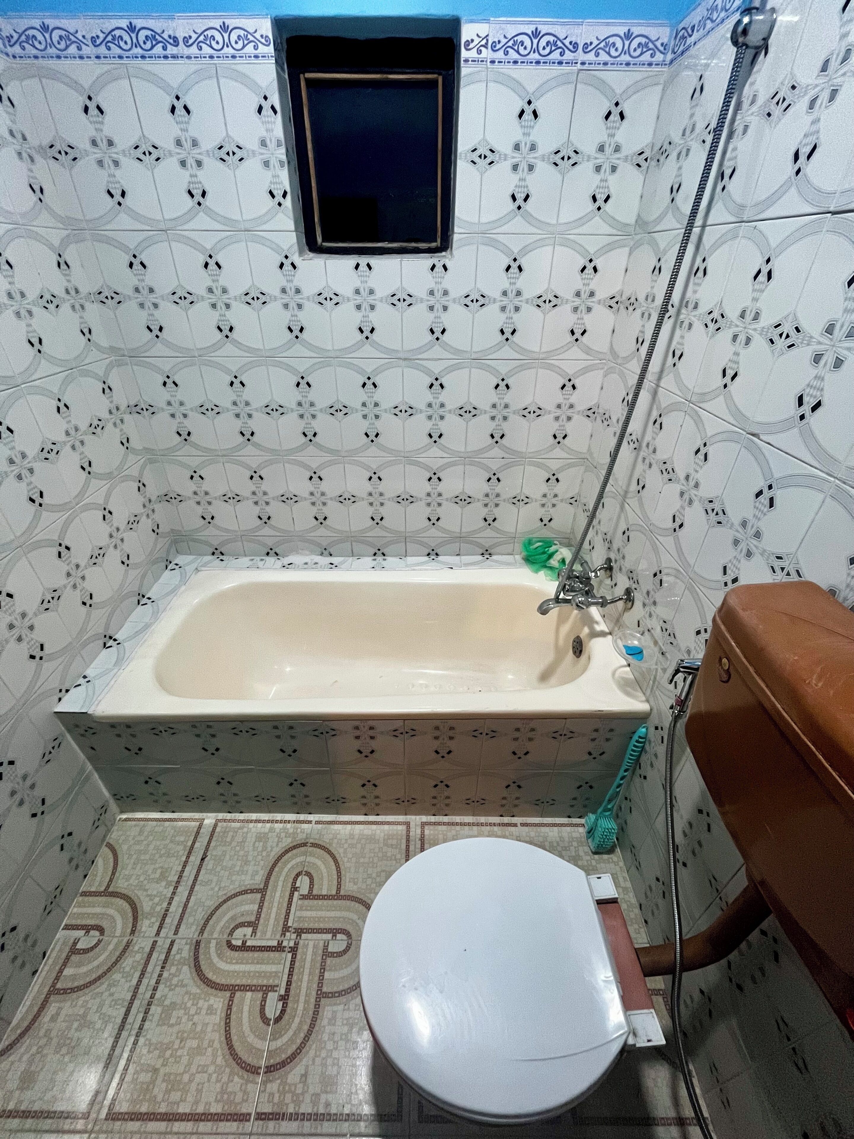 Een badkamer met een bad, toilet en een klein raam.