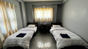 A room with two single beds, a small table, and a window with curtains.