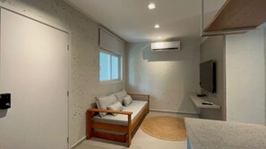 A small, compact room with a single bed, a window, a wall-mounted air conditioner, and a television. - São Miguel dos Milagres, Praia do Marcineiro. New condominium near the town center. (São Miguel dos Milagres)