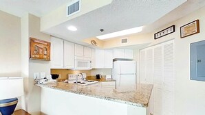 A kitchen with white cabinets, a granite countertop, a microwave, a stove, and a refrigerator. - Carolinian Beach Resort 1735 (Myrtle Beach)