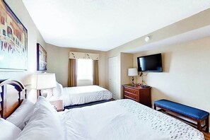 Ett hotellrum med två sängar, en tv, ett skrivbord med en lampa och ett fönster med gardiner.