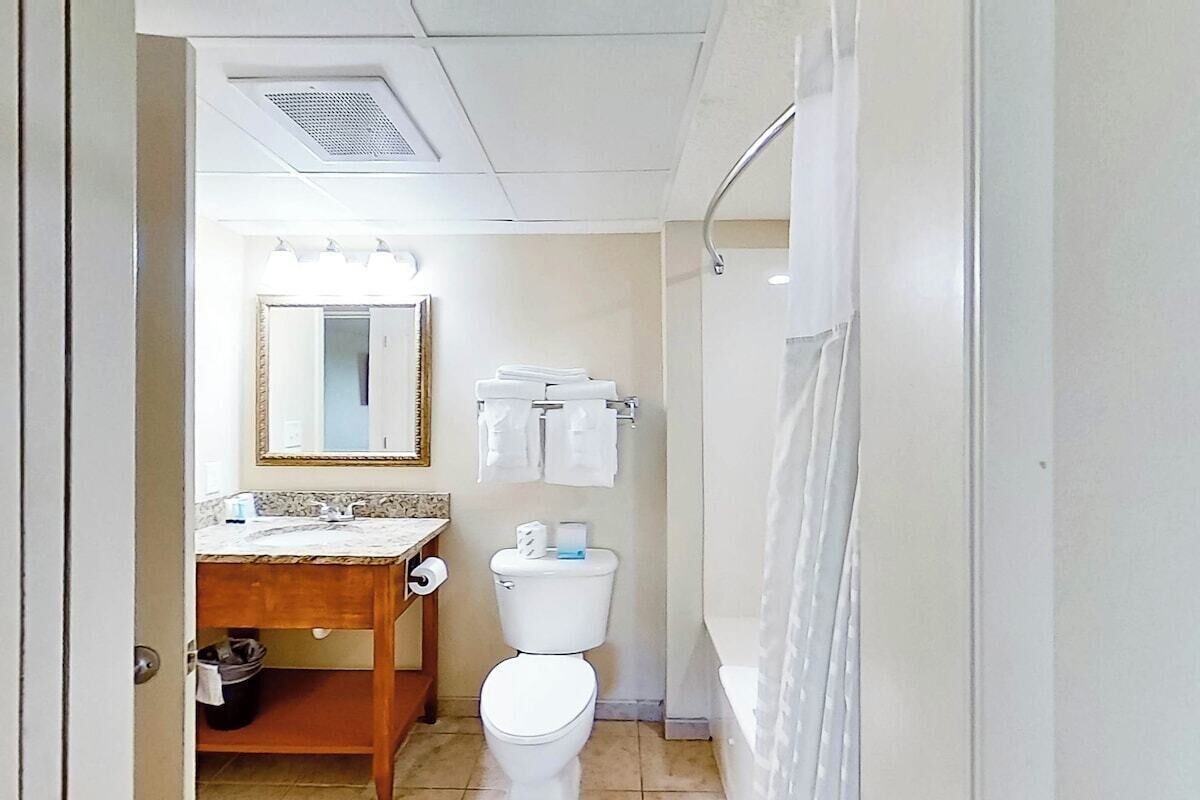 A bathroom with a toilet, sink, mirror, and towel rack.