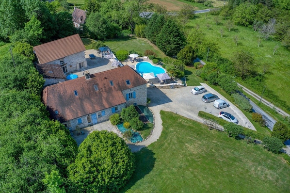 A large house with a swimming pool, multiple cars, and a well-maintained lawn.