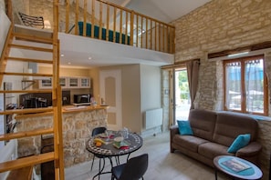 A loft-style living area with a dining table, a sofa, and a staircase leading to a loft bedroom. - Hostcare - La Salamandre – swimming pool (Carlux)