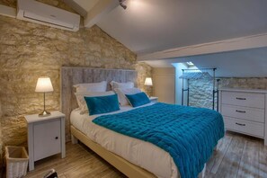 A bedroom with a stone wall, a bed with a teal duvet, bedside lamps, and a hanging clothes rack.