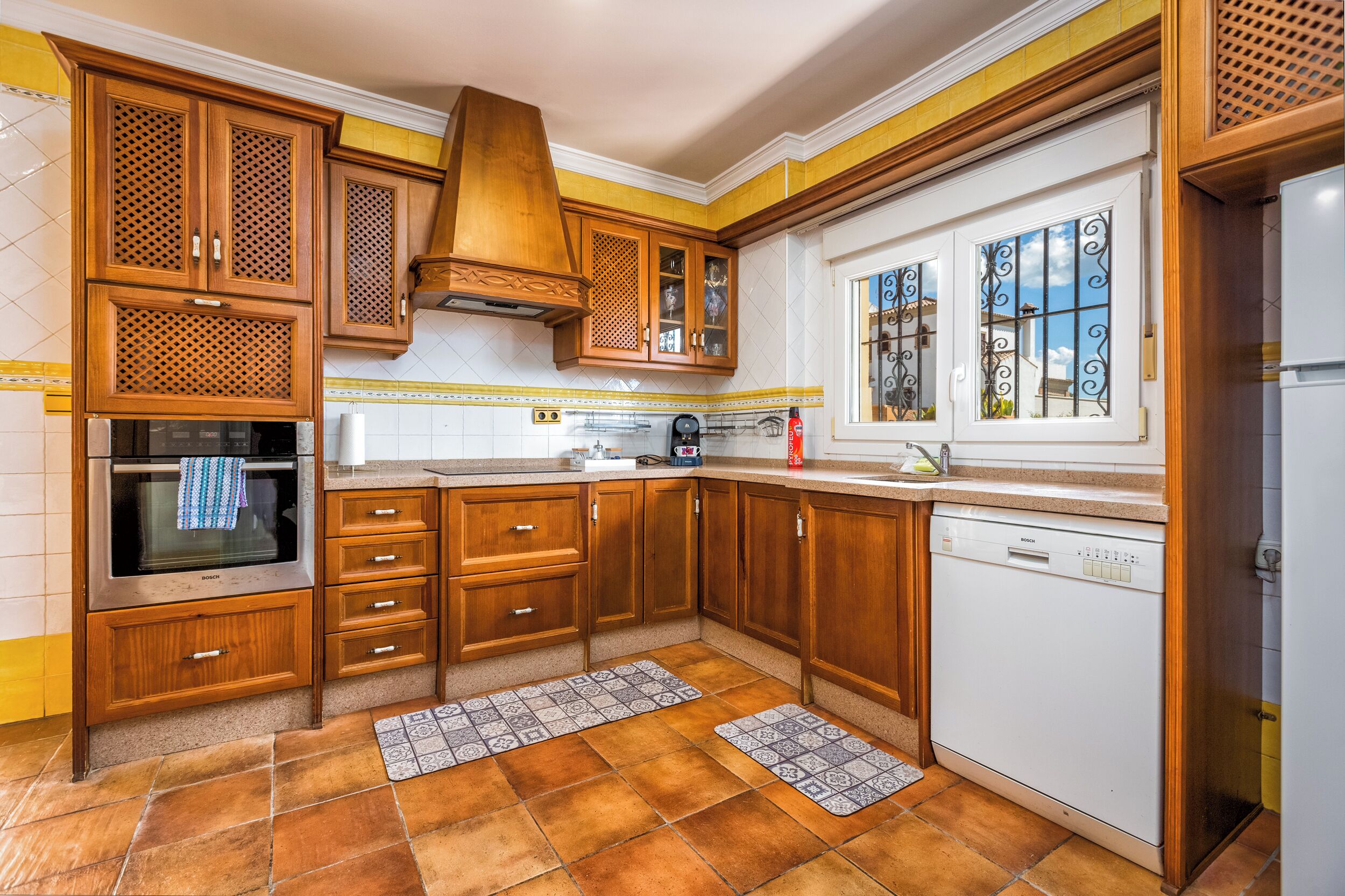 A kitchen with wooden cabinets, a Bosch dishwasher, and a window with decorative iron bars.