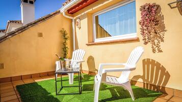 Une terrasse avec deux chaises blanches, une petite table et une bouteille de champagne.