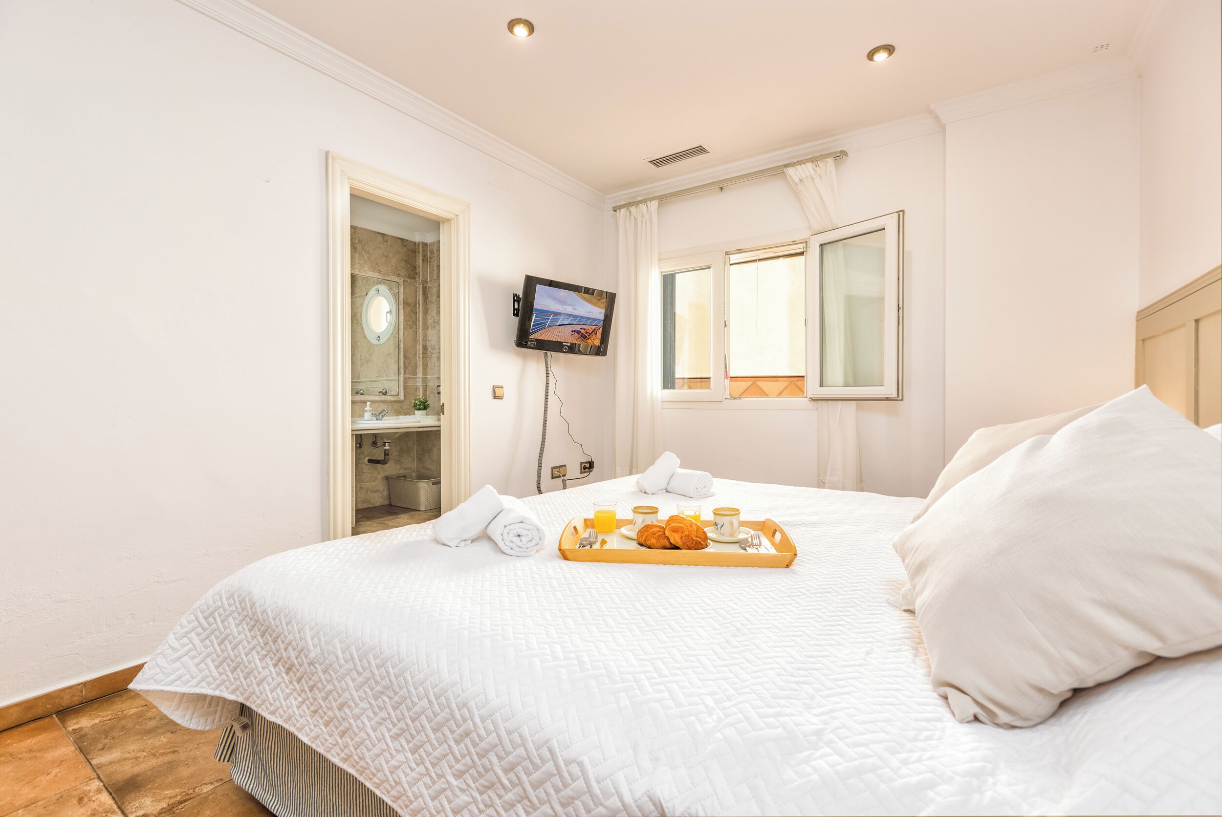 A hotel room with a bed, a TV, a window, and a breakfast tray.