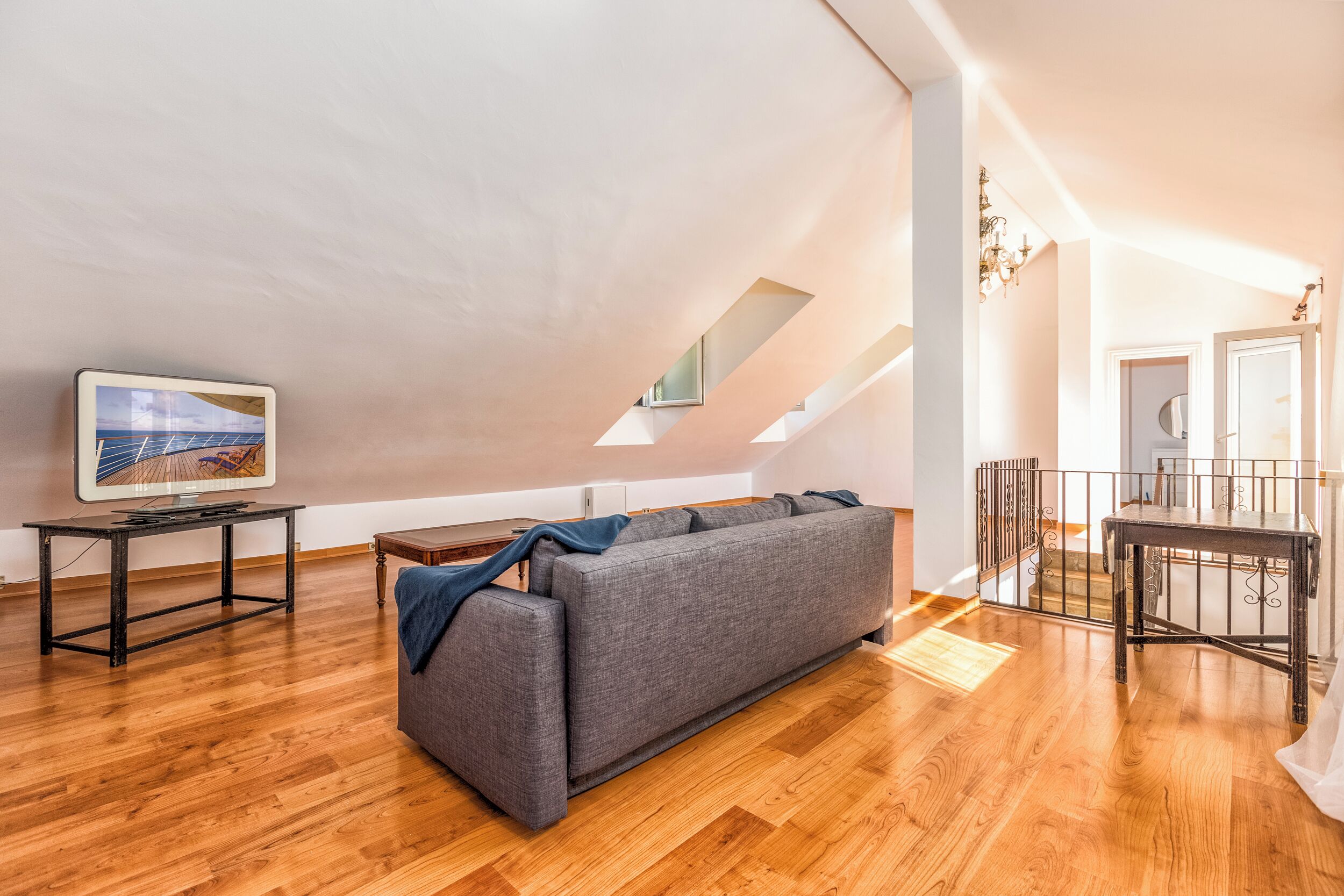 A modern loft apartment with a high ceiling, a grey sofa, a wooden floor, and a television on a table.