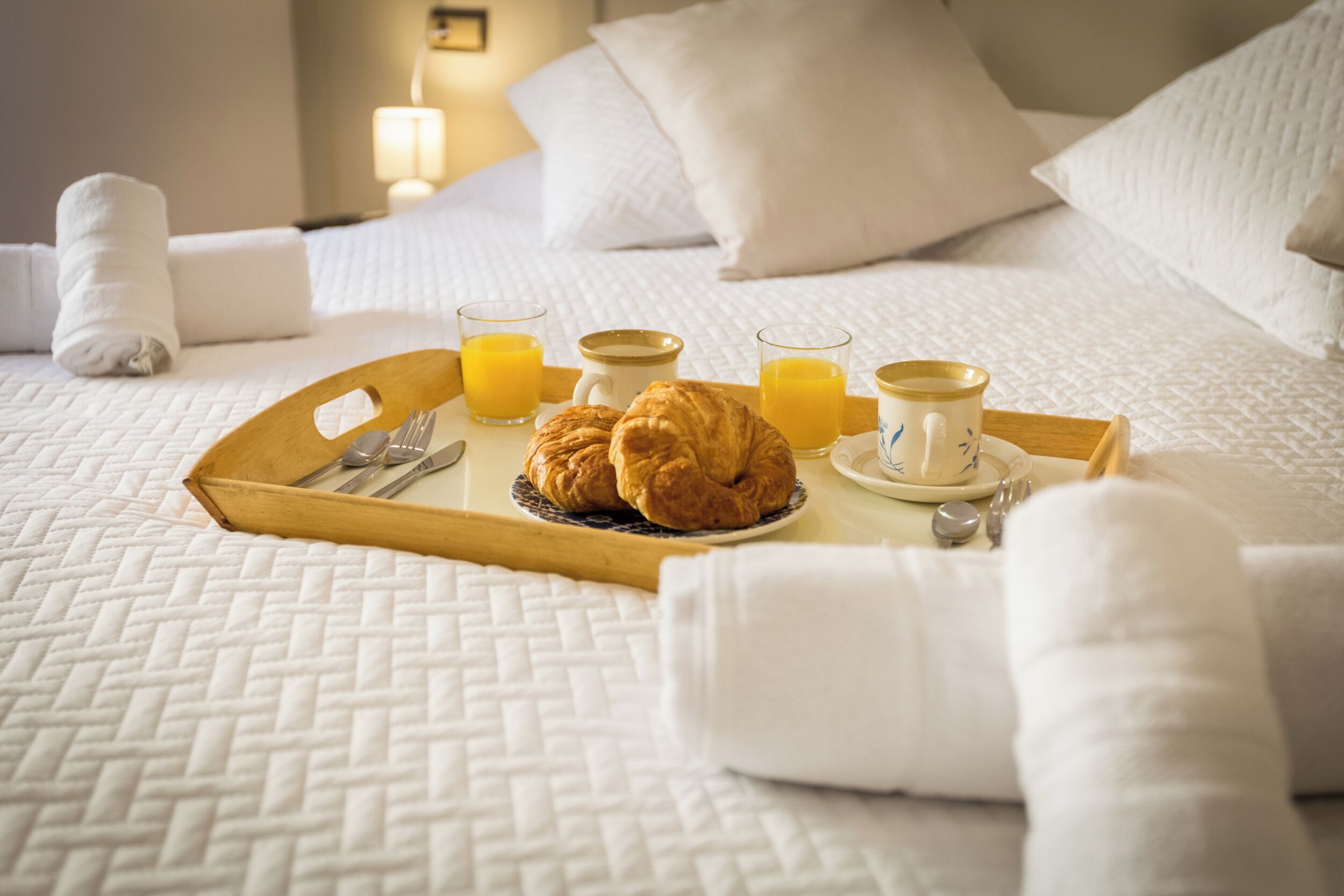 A neatly made bed with a tray of breakfast items including croissants, juice, and coffee.