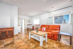 A living room with a wooden coffee table, a leather sofa, and a dining area with a white tablecloth.