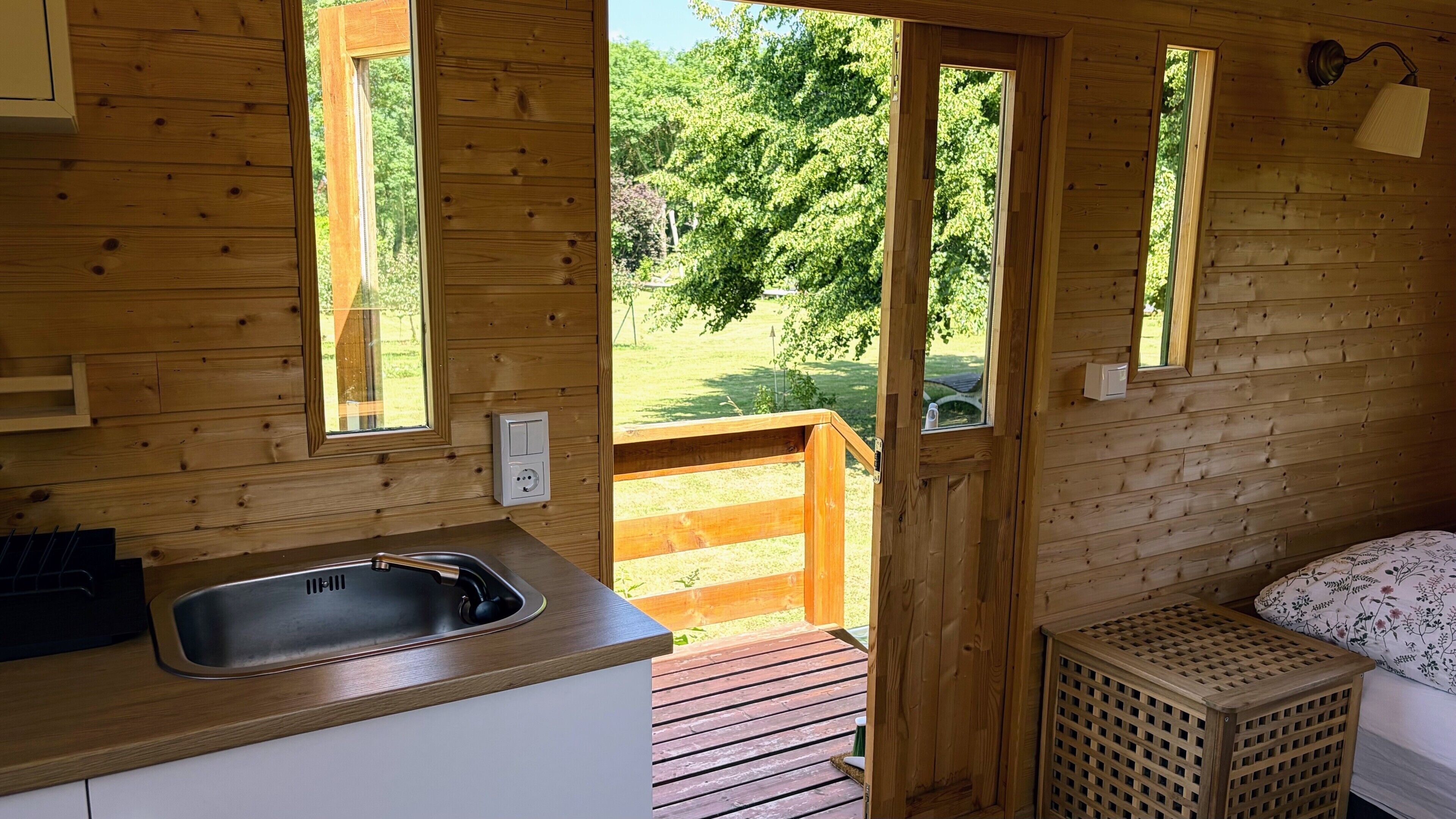 A wooden cabin with a kitchen area, a sink, and a window overlooking a green landscape.