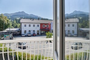 Ein Gebäude mit roter und weißer Fassade, ein Parkplatz mit mehreren Autos und eine gebirgige Landschaft im Hintergrund.