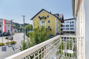 En gul bygning med balkon, en gade med biler og flag.