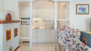 Ett kompakt bostadsutrymme med ett litet kök, en soffa med ett blommönster och ett inramat konstverk på väggen.