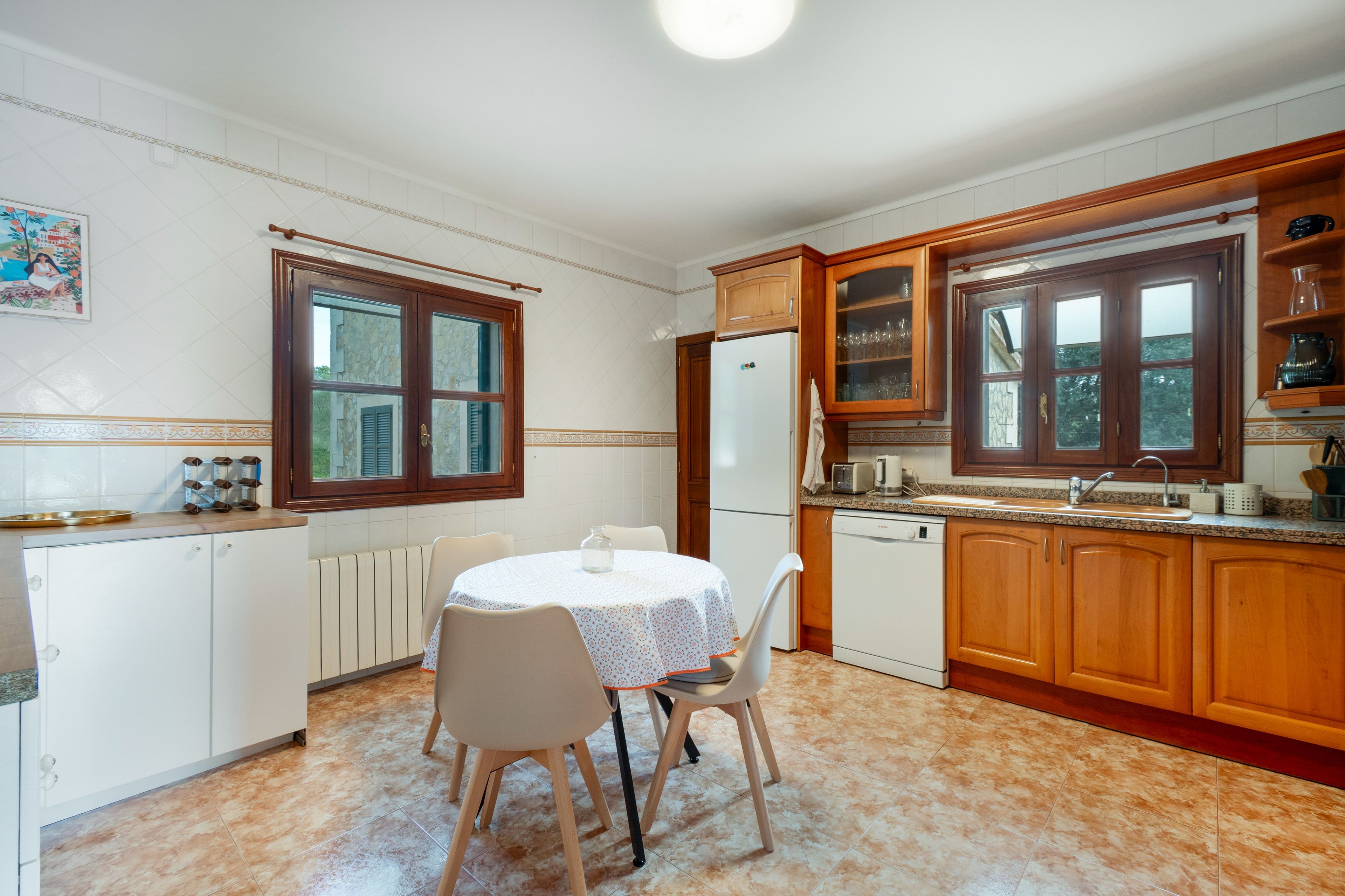 Eine Küche mit Esstisch, Stühlen, Holzschränken, einem Kühlschrank und einem Fenster.