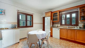 Eine Küche mit Esstisch, Stühlen, Holzschränken, einem Kühlschrank und einem Fenster.
