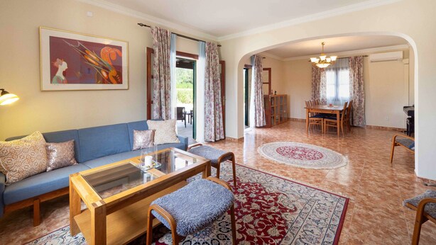 A living room with a sofa, coffee table, and chairs, a dining area with a table and chairs, and a hallway leading to an outdoor area.
