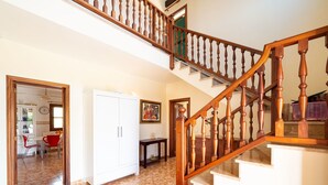 A spacious living area with a wooden staircase, a dining area with red chairs, and a white wardrobe.