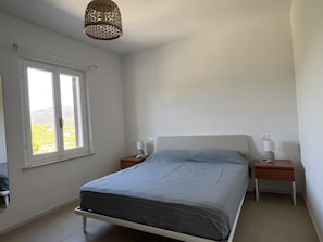 Ein Schlafzimmer mit einem Bett, zwei Nachttischen, einem Fenster und einer Pendelleuchte.