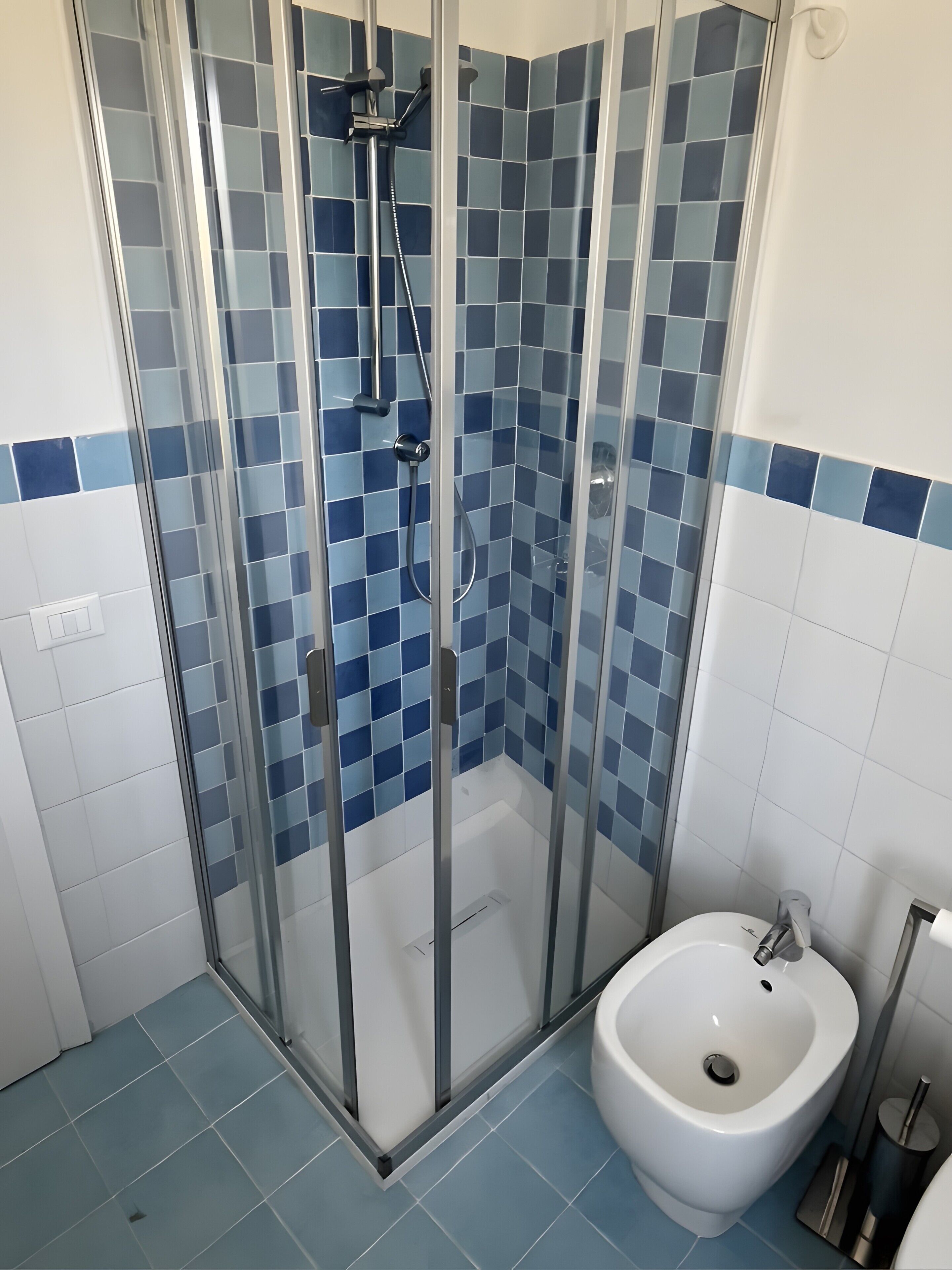 Un bagno con doccia vetro, bidet e pareti in piastrelle blu.
