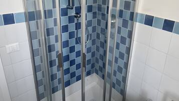 Un bagno con doccia vetro, bidet e pareti in piastrelle blu.