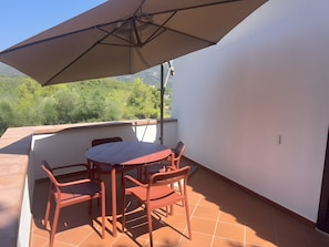 Eine Terrasse mit Tisch, Stühlen und einem Sonnenschirm, mit Blick auf Grünflächen.
