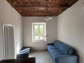 Ein Zimmer mit Ziegeldecke, einem Fenster mit Aussicht, einem blauen Sofa und einem Tisch.