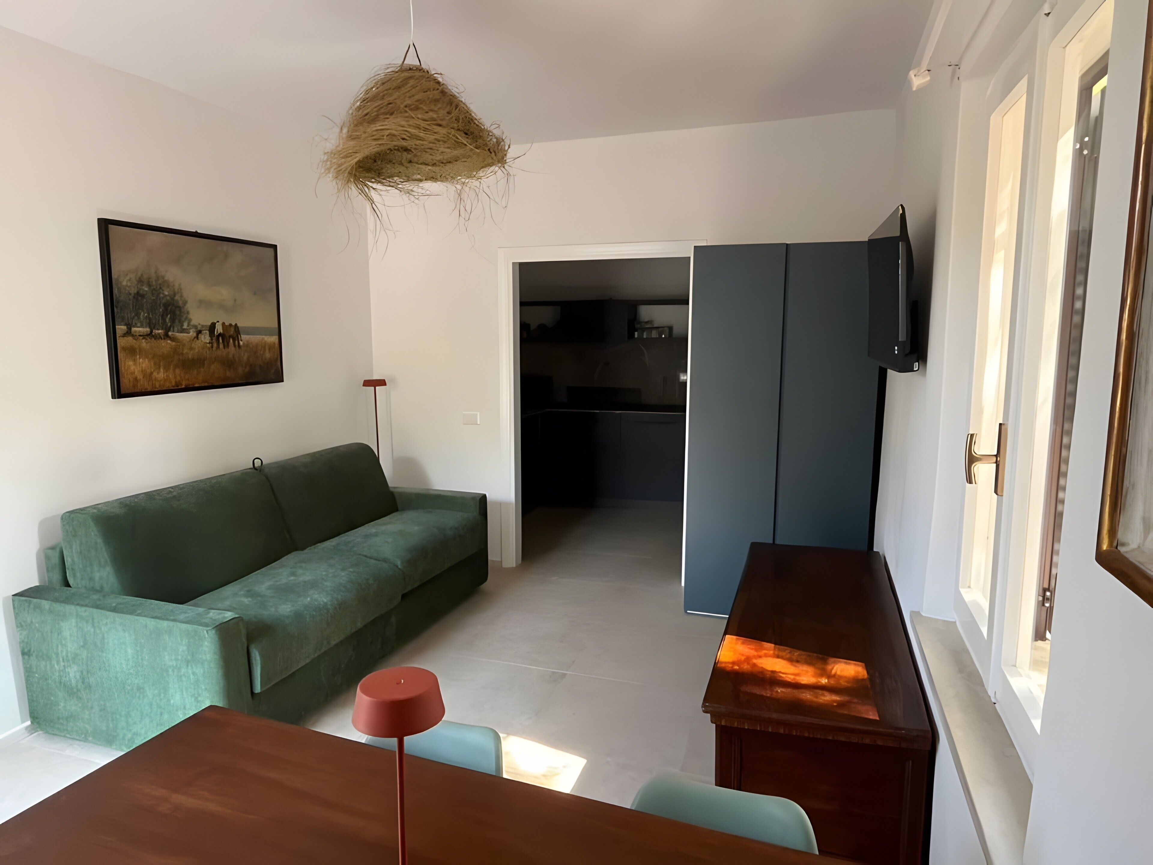 A living room with a green sofa, a wooden coffee table, a hanging light fixture, and a painting on the wall.